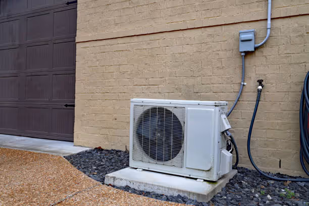 White mini-split air conditioning unit installed on brick wall near garage