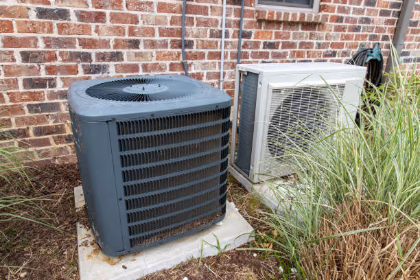 Two air conditioning units sitting on concrete pads next to brick wall