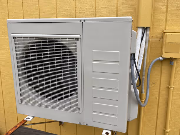 Gray air conditioning unit mounted on yellow wooden exterior wall
