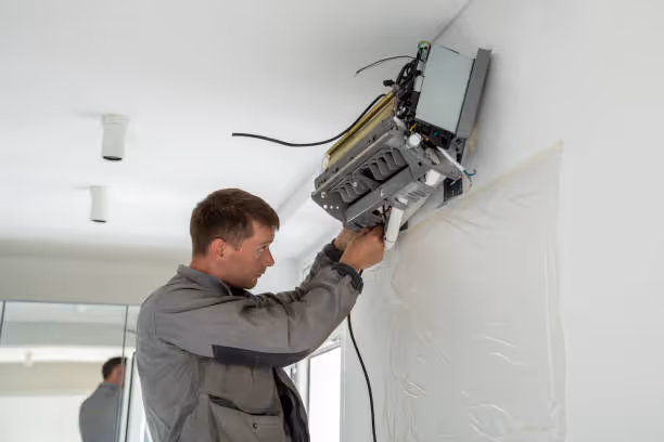 Technician installing security camera on white wall with cable connection