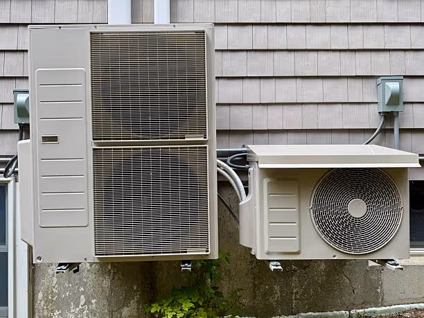 Two outdoor HVAC units mounted on concrete wall with siding background