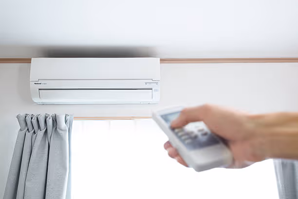 Hand using remote control to operate wall-mounted air conditioning unit