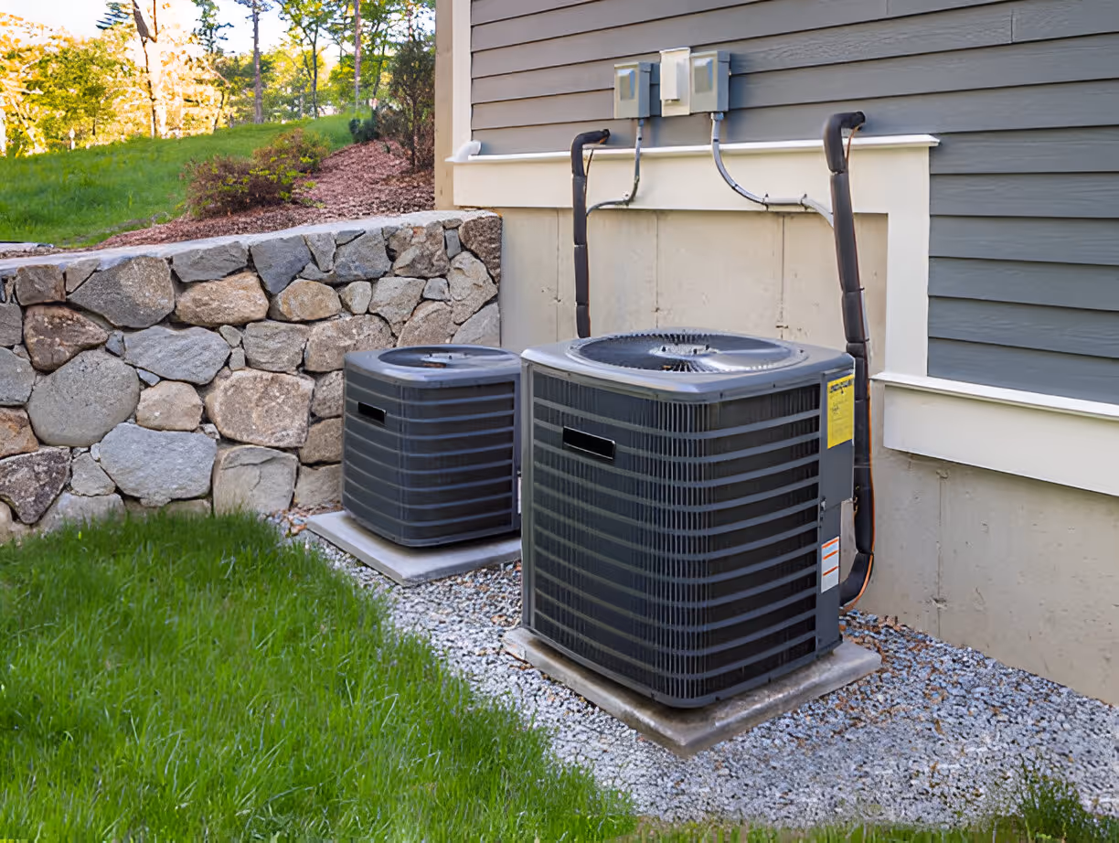 Two air conditioning units sit near stone wall and green lawn