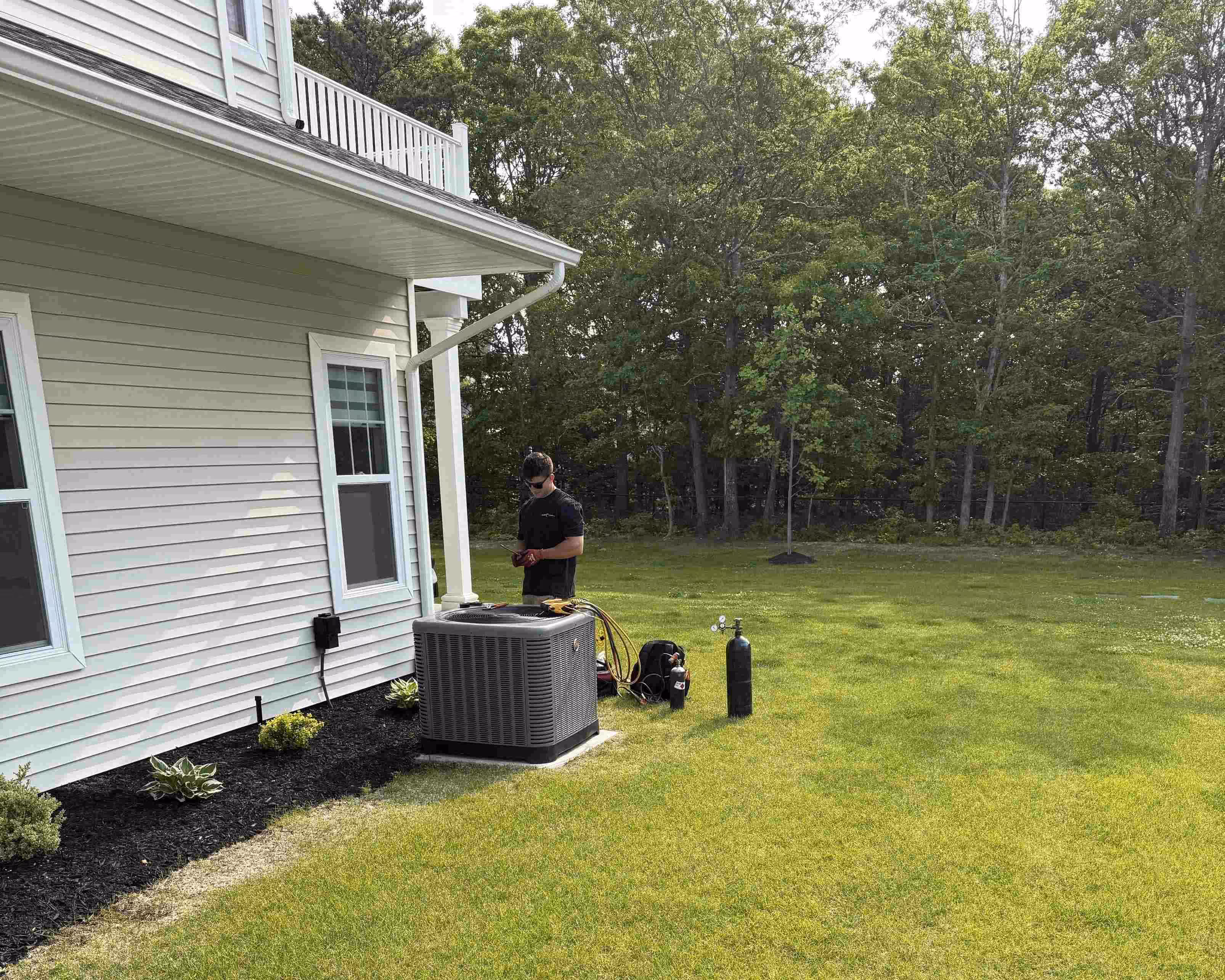 Technician servicing outdoor air conditioning unit next to white house
