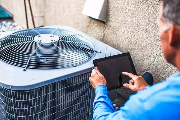 Technician using tablet while checking outdoor HVAC unit