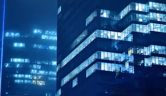Modern commercial building illuminated with vibrant lights at night, showcasing architectural design and urban atmosphere.

