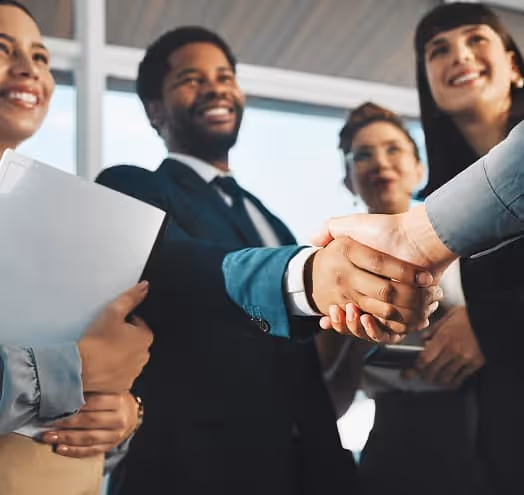 A diverse team gathered in a professional setting, shaking hands with a central team member to signify collaboration and success.