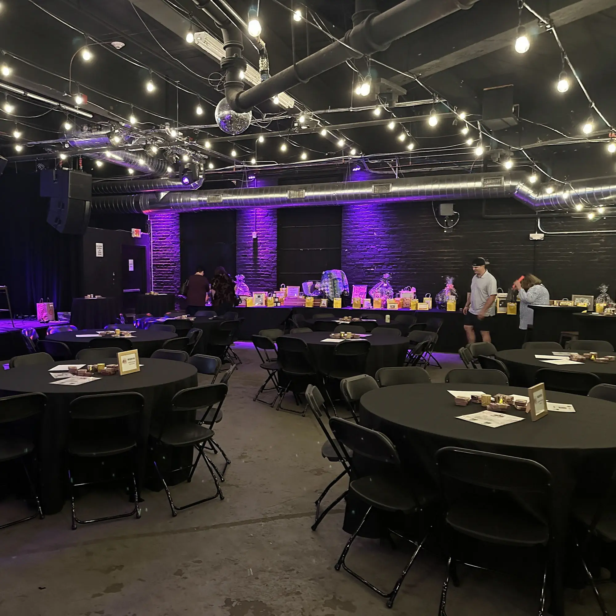 Round tables set up in the main room under string lights at Taffeta Music Hall