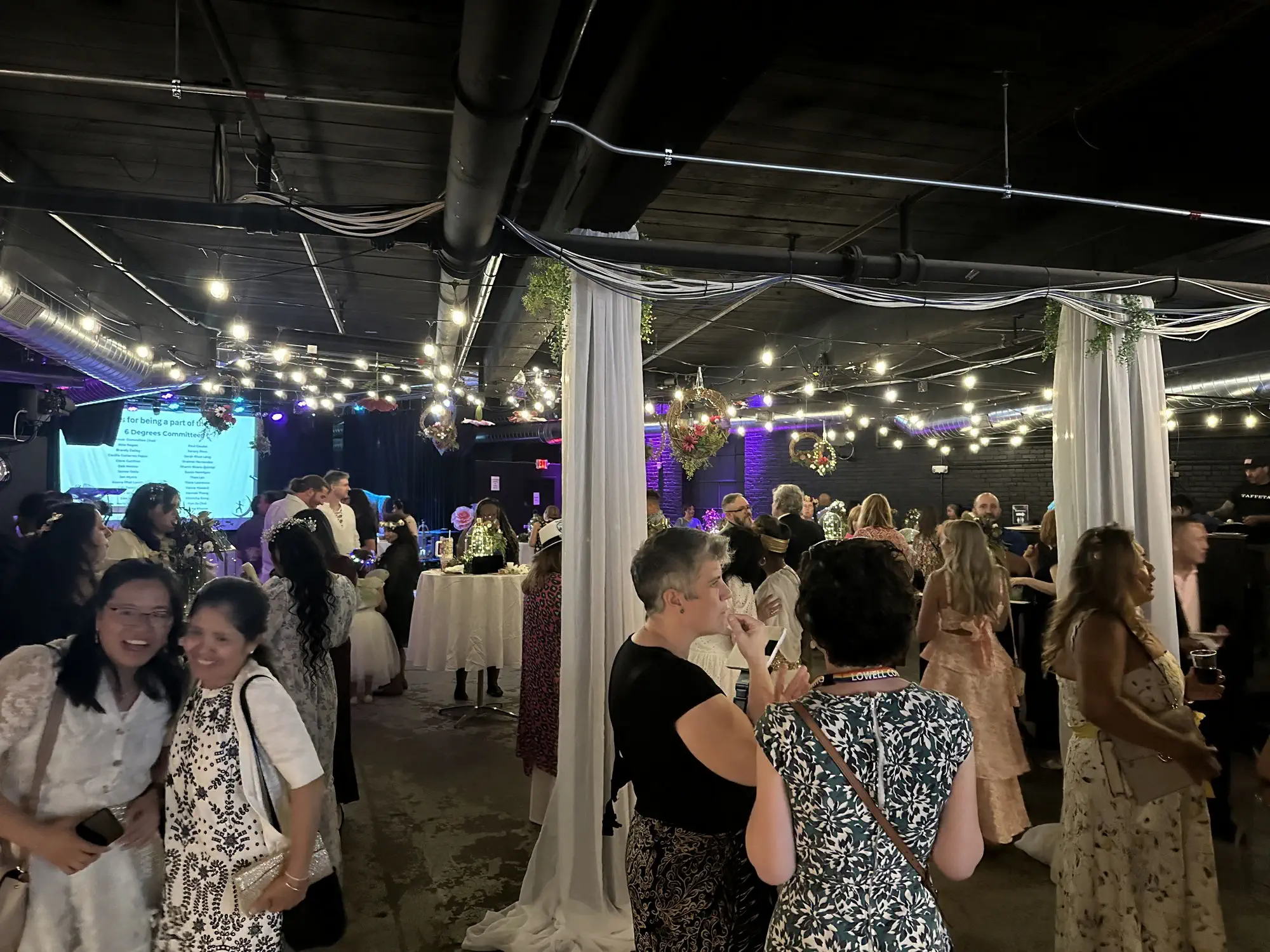 Guests at a formal party among draped columns and string lights at Taffeta Music Hall