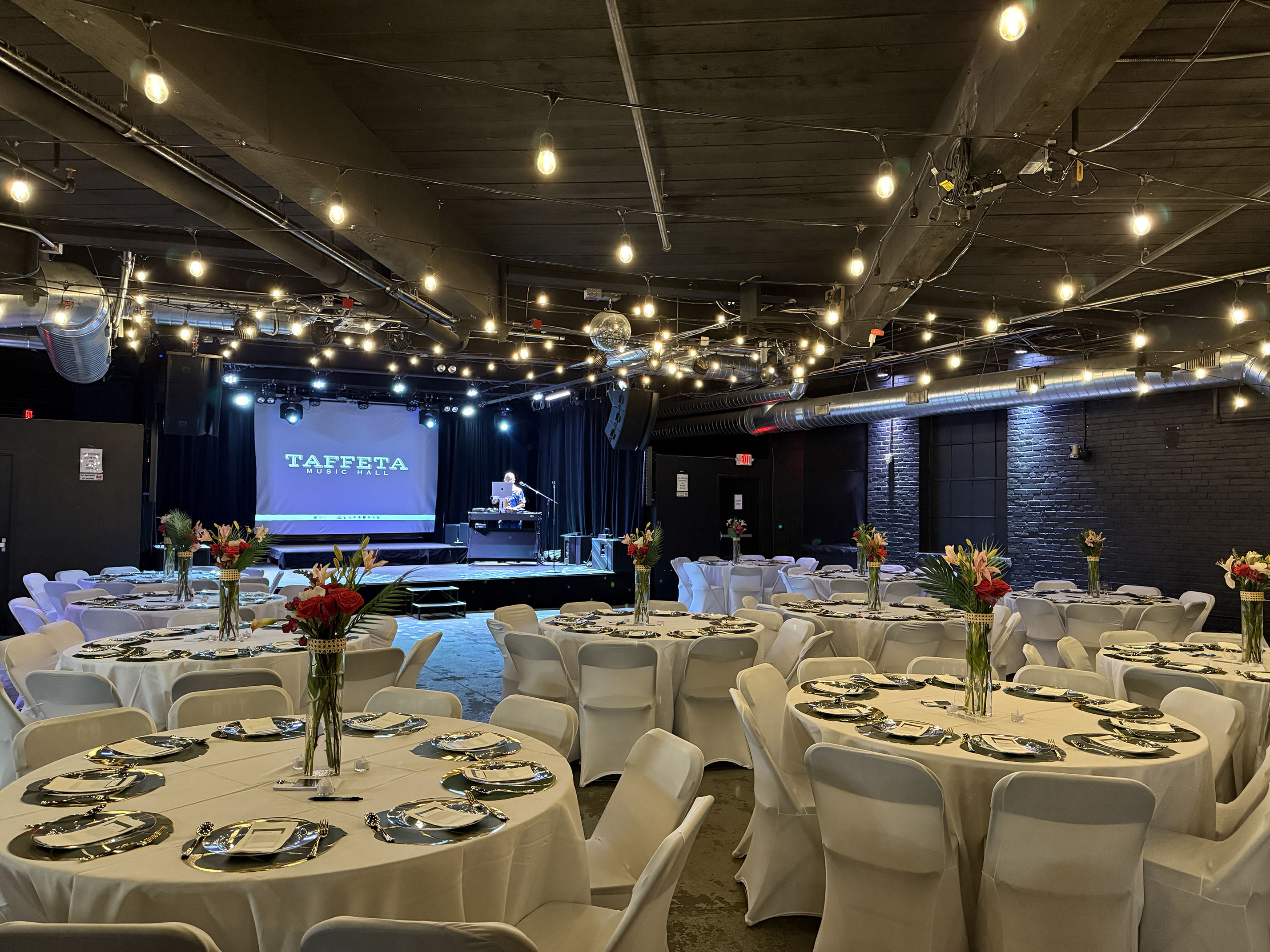 Round tables with white linens and floral centerpieces facing the stage at Taffeta Music Hall