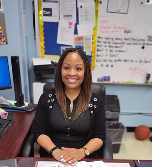 K. Smith smiling at desk in classroom setting