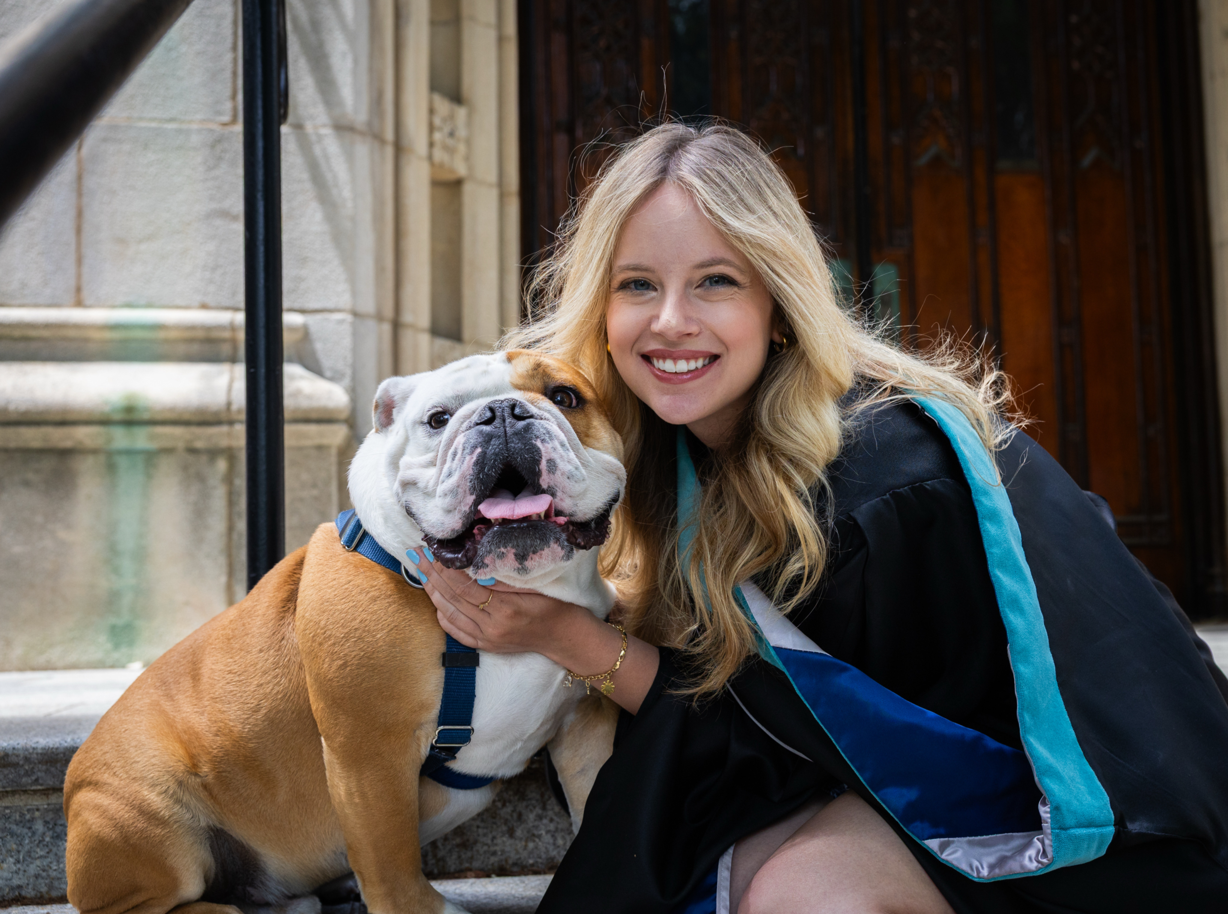 Young blonde woman stands on University campus on a sunny day in a black turtleneck top