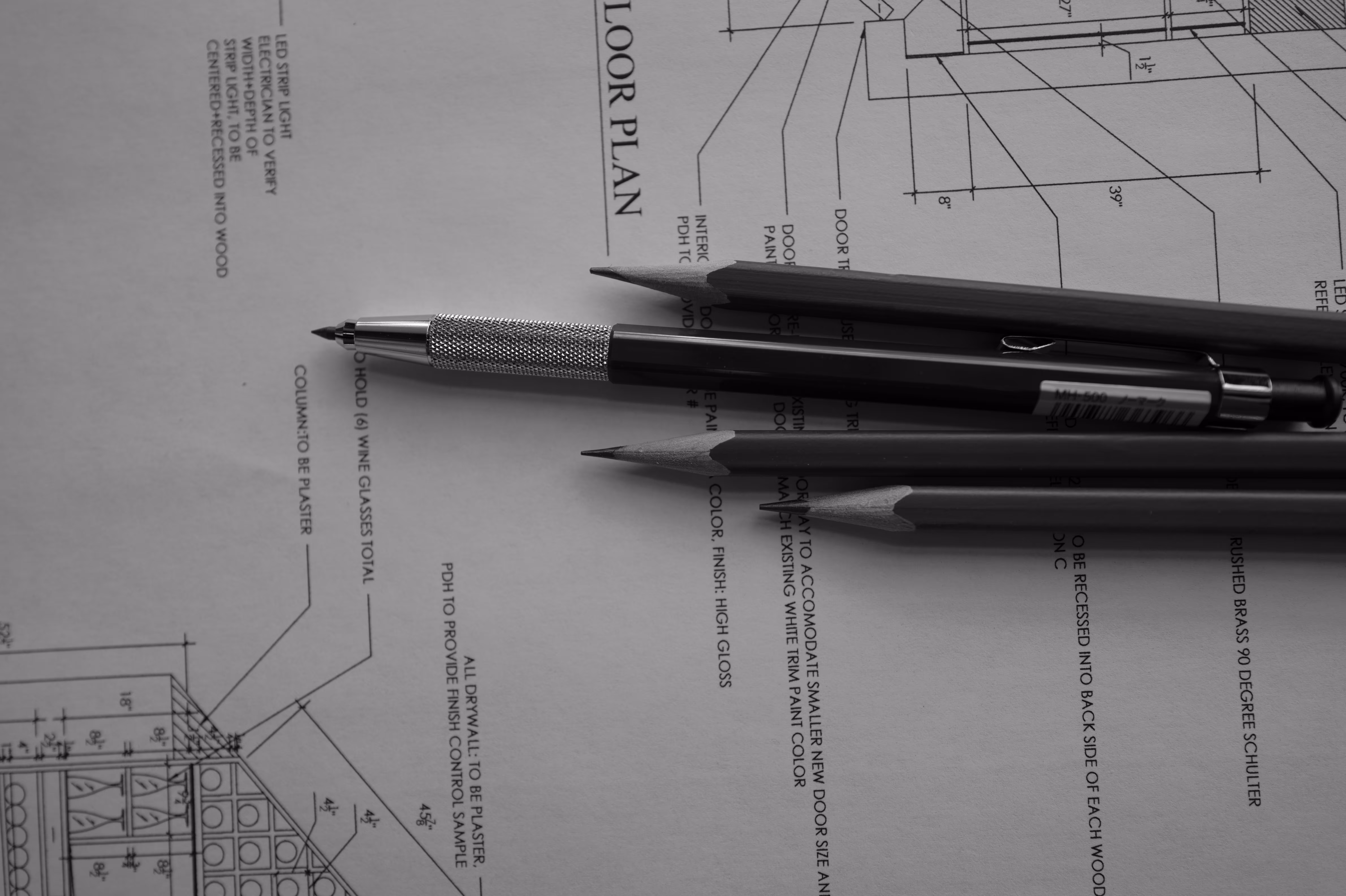Mechanical pencil and three wooden pencils lying on a floor plan architectural blueprint.