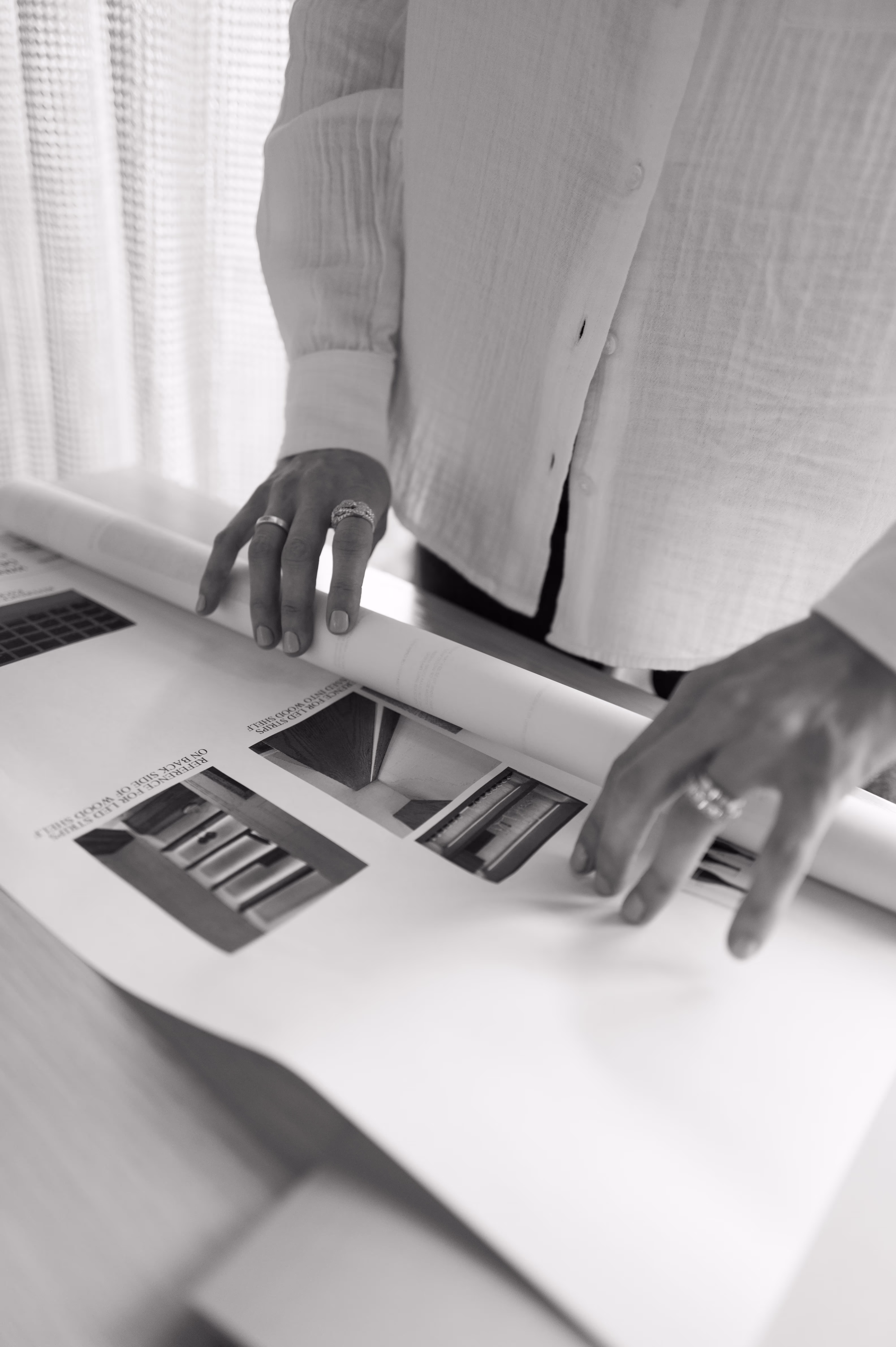 Person wearing rings rolling up a large architectural blueprint on a wooden table.