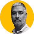 Portrait of a middle-aged man with gray hair and beard against a yellow background.