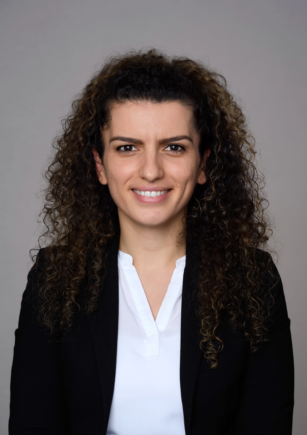 Professional headshot of a woman with long curly brown hair smiling at camera