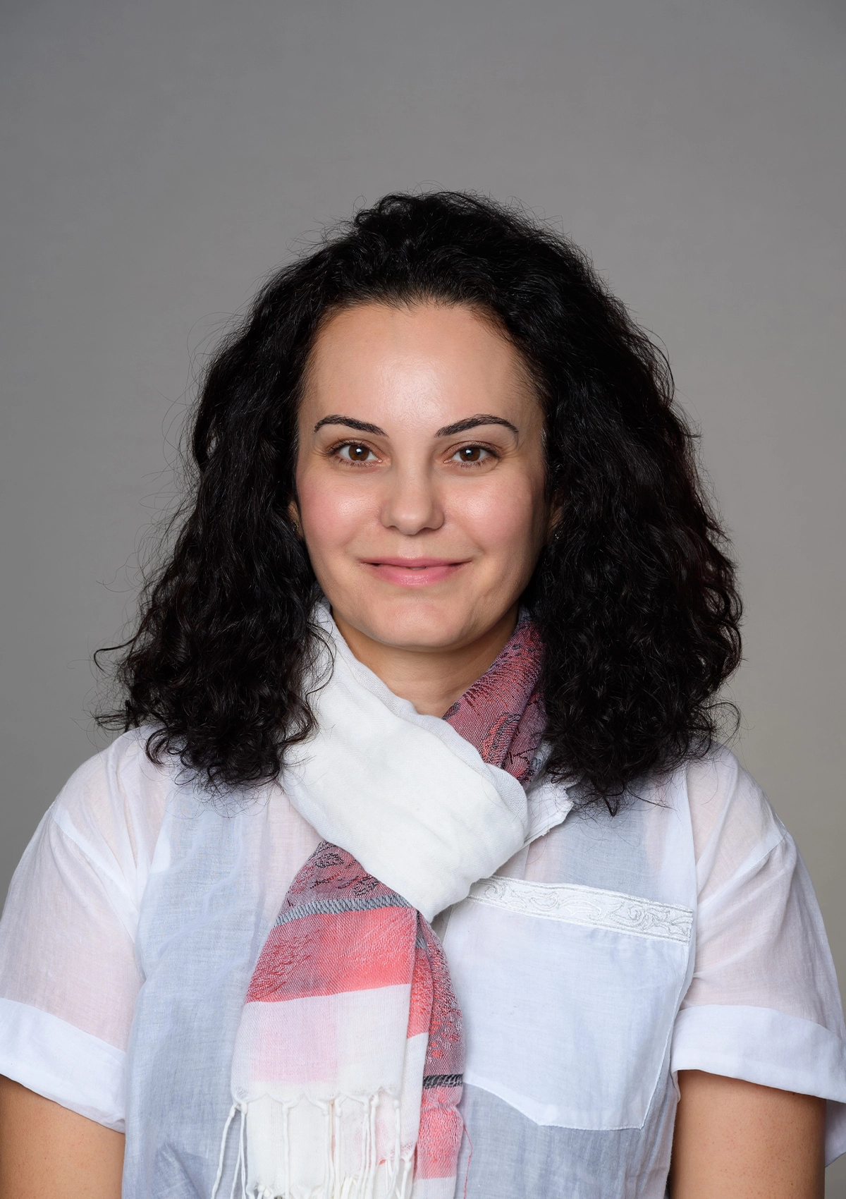 Portrait of woman with long dark curly hair wearing light blue shirt and scarf