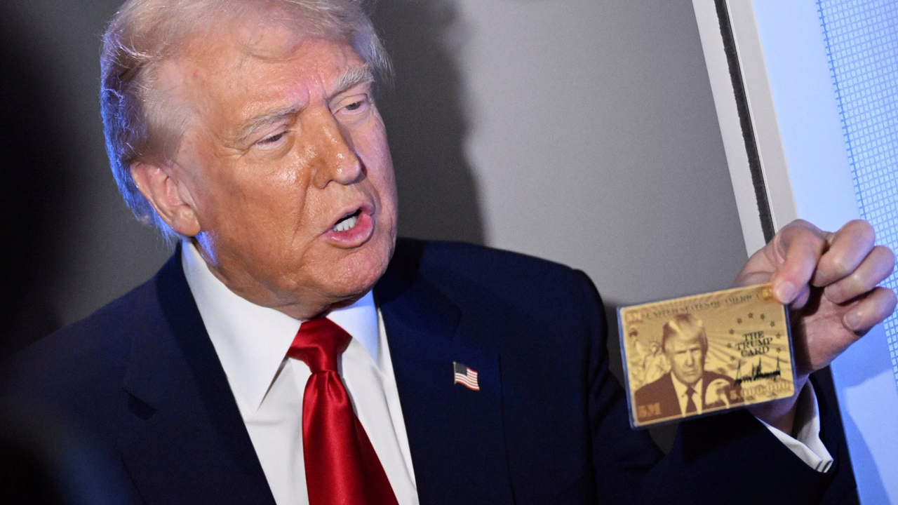 Man in dark suit and red tie holding and displaying a commemorative gold card