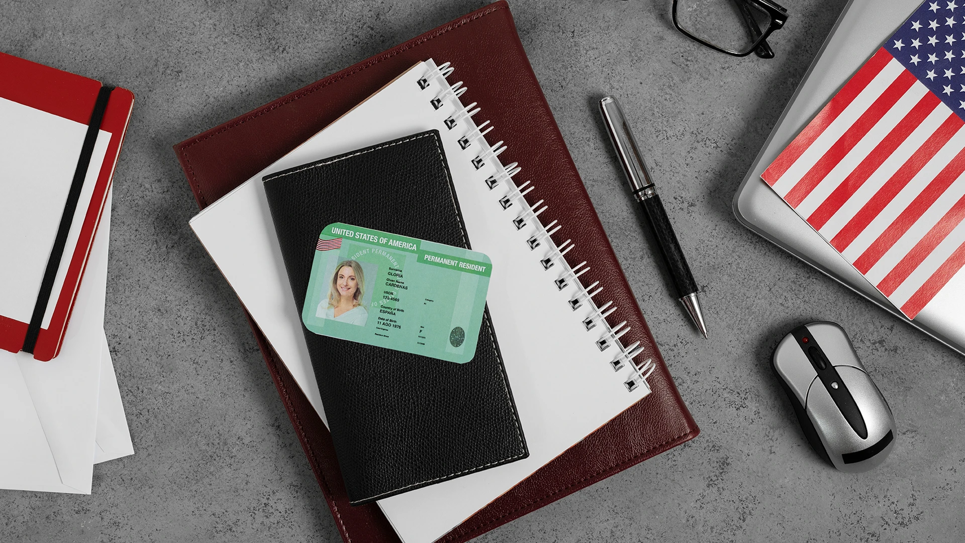Green permanent resident card displayed on black wallet with notebooks and American flag items