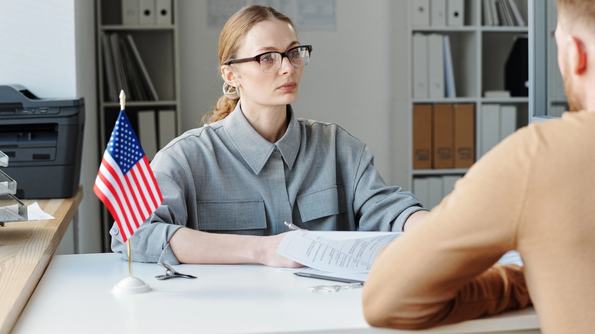 Woman wearing glasses sits at desk with American flag during professional office meeting