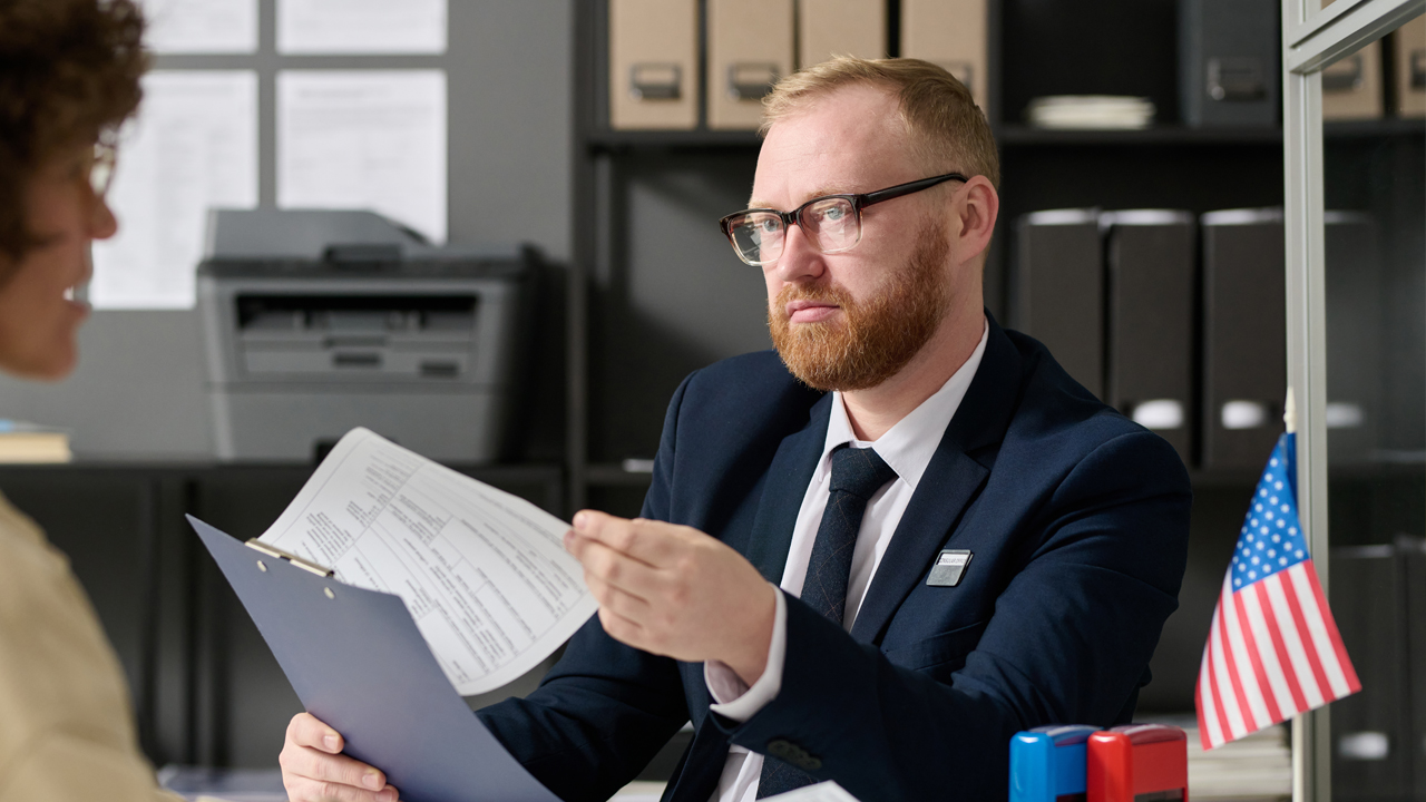 Businessman in navy suit and glasses reviews documents at office desk