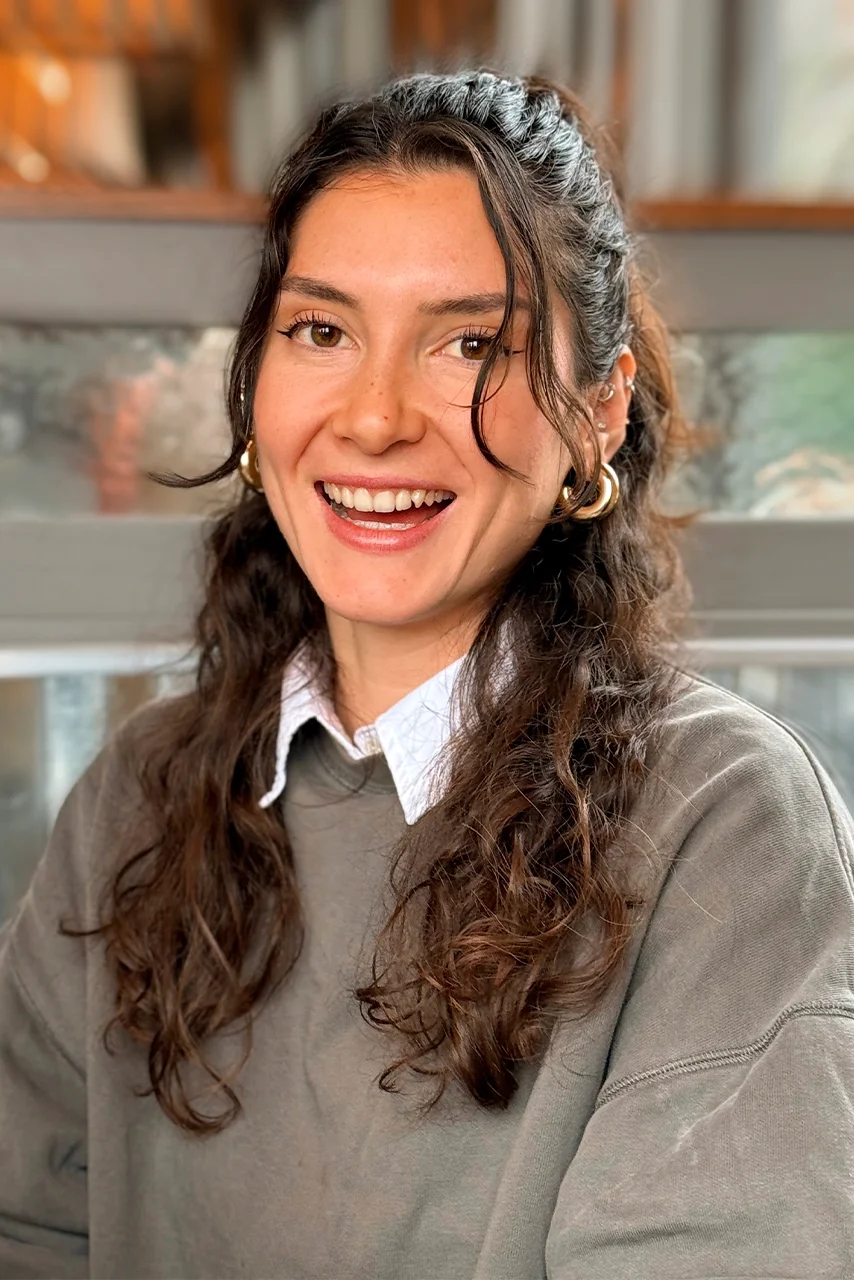 Smiling woman with long dark hair wearing gray sweater and white collar