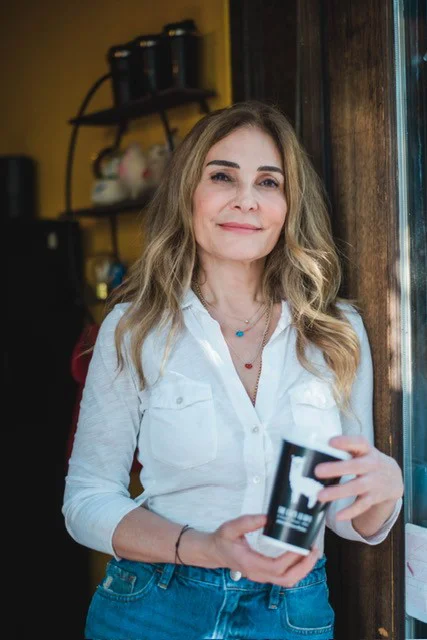 Woman in white shirt holding camera near rustic wooden wall indoors