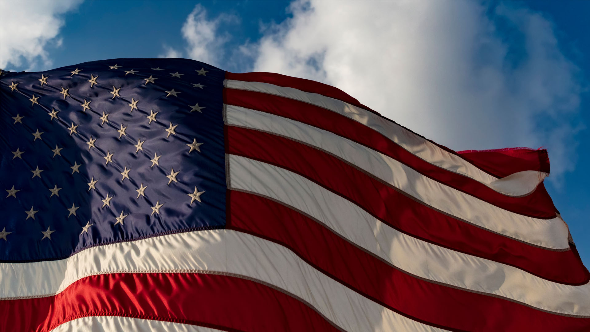 American flag waving against a blue sky with clouds, anti-Americanism and US immigration policy