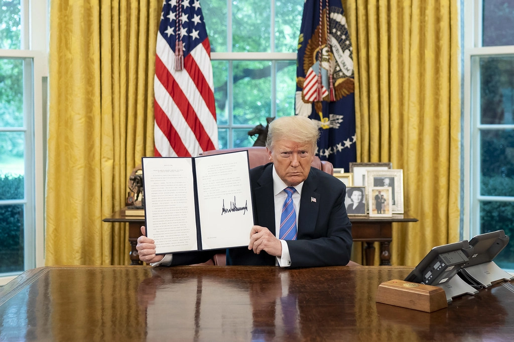 President Trump holds a signed executive order in the Oval Office, navigating US immigration policy changes