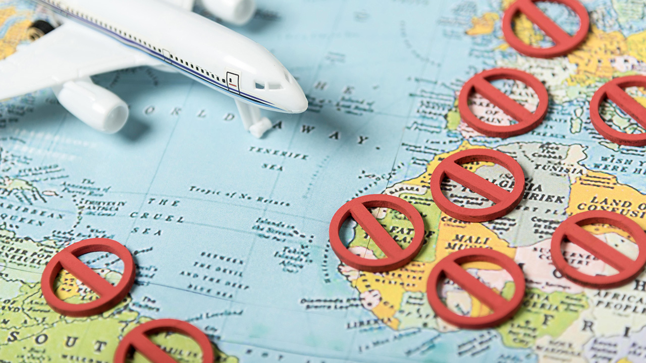 Toy plane on a world map dotted with red prohibition signs, decision pause for travel ban countries