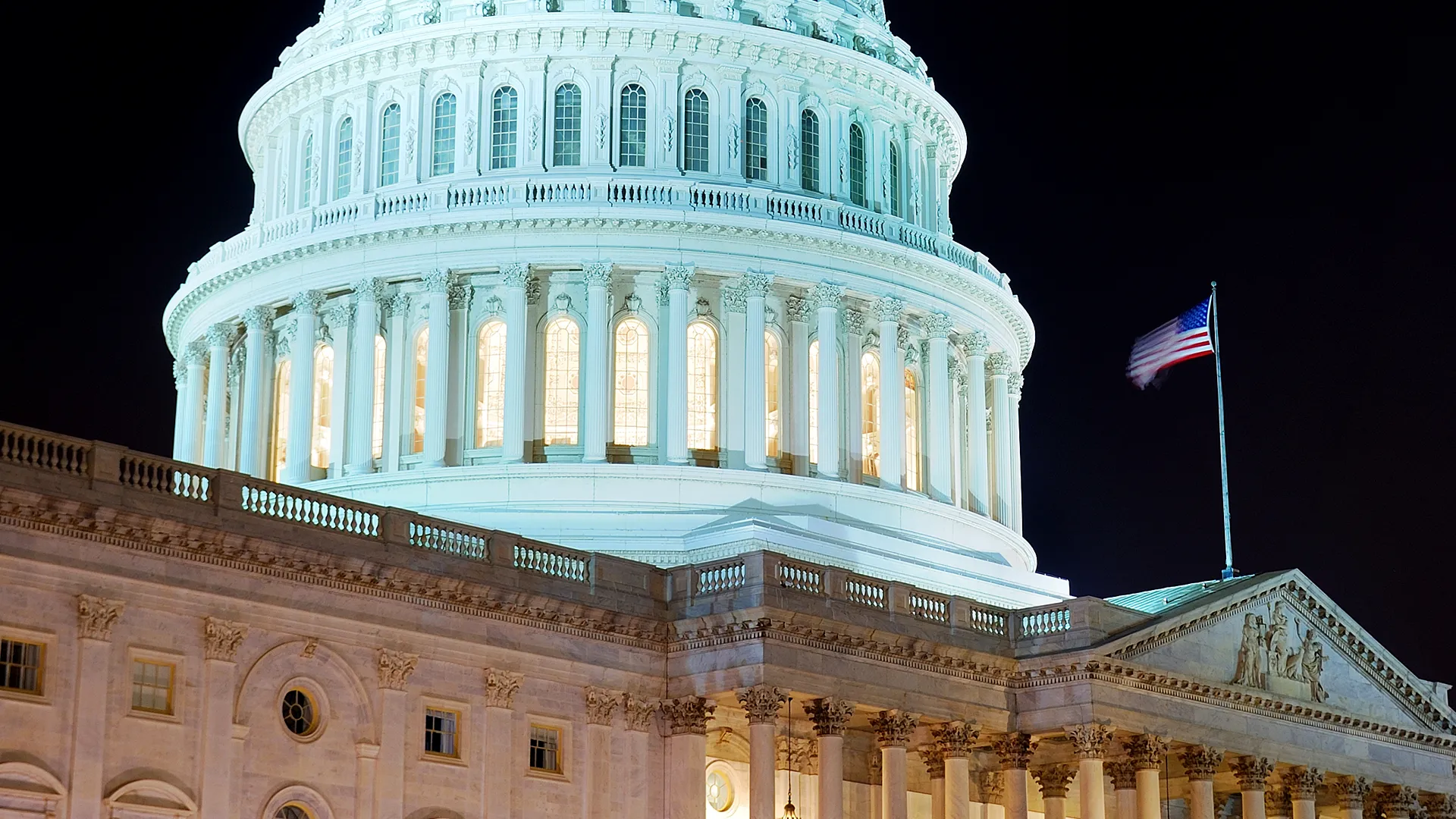 US Capitol dome lit at night with American flag, Senate passes 150 billion dollar immigration enforcement bill