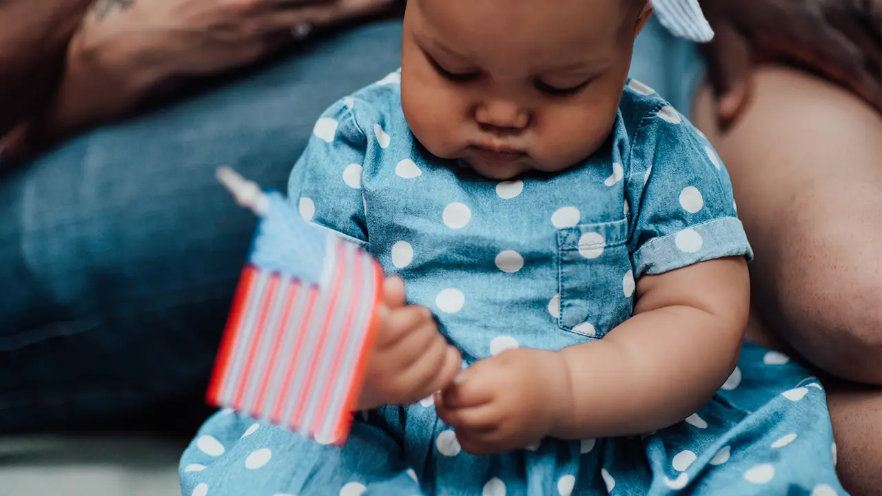 Baby in a polka dot dress holds a small American flag, Supreme Court upholds birthright citizenship