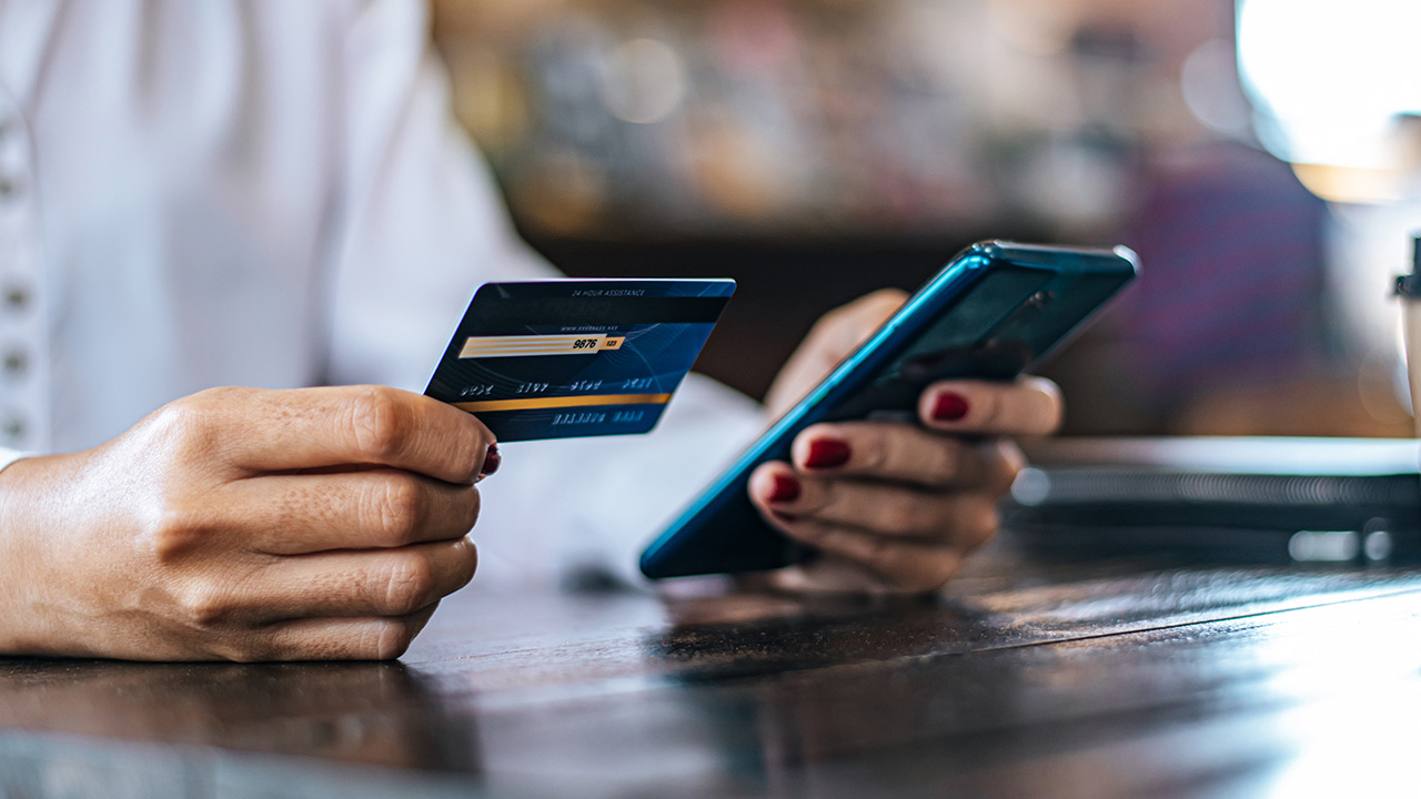 Hands holding a credit card and phone to pay online, USCIS electronic payments for filing fees
