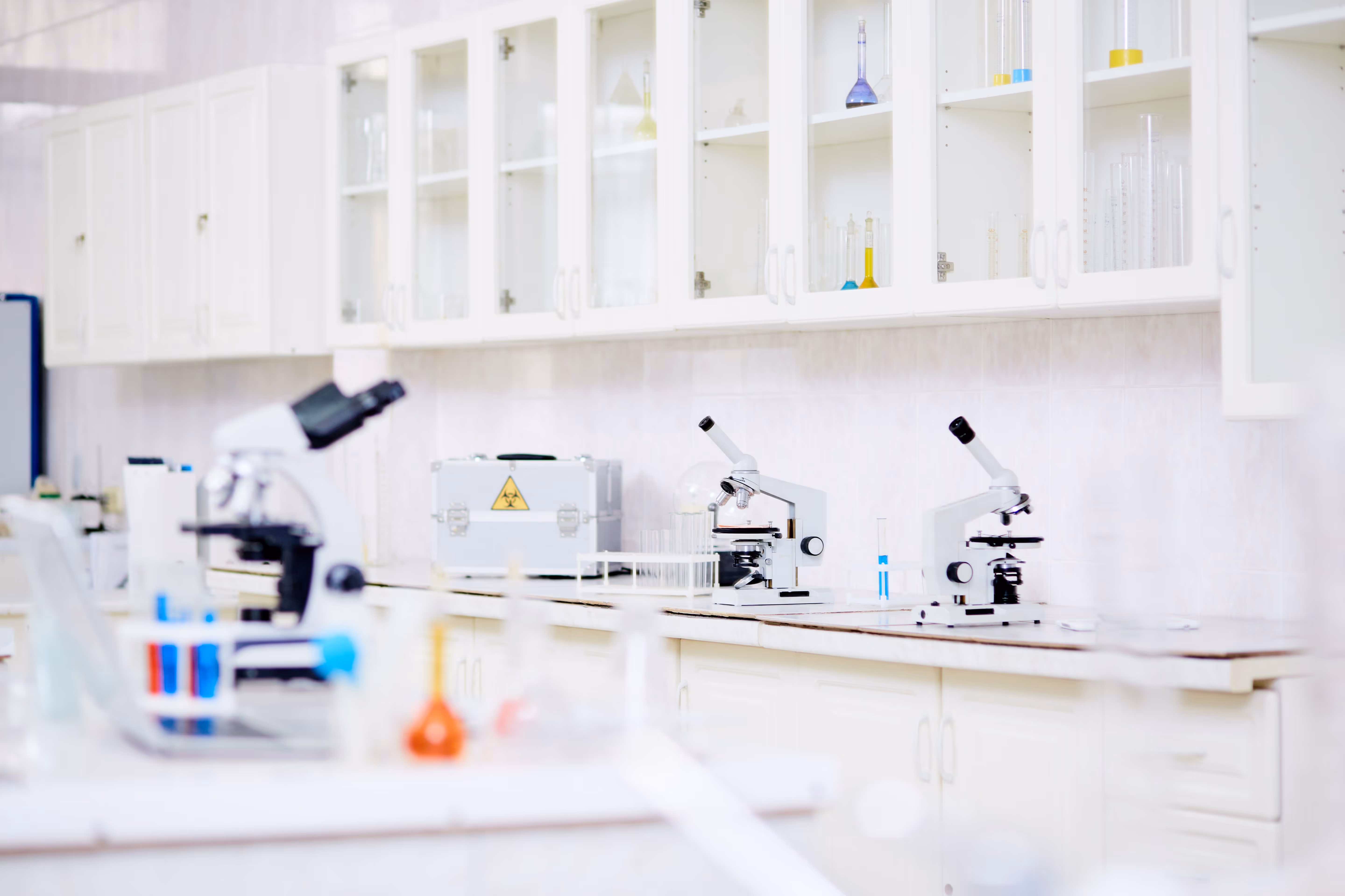 Laboratoire blanc avec microscopes et verrerie chimique sur les plans de travail.