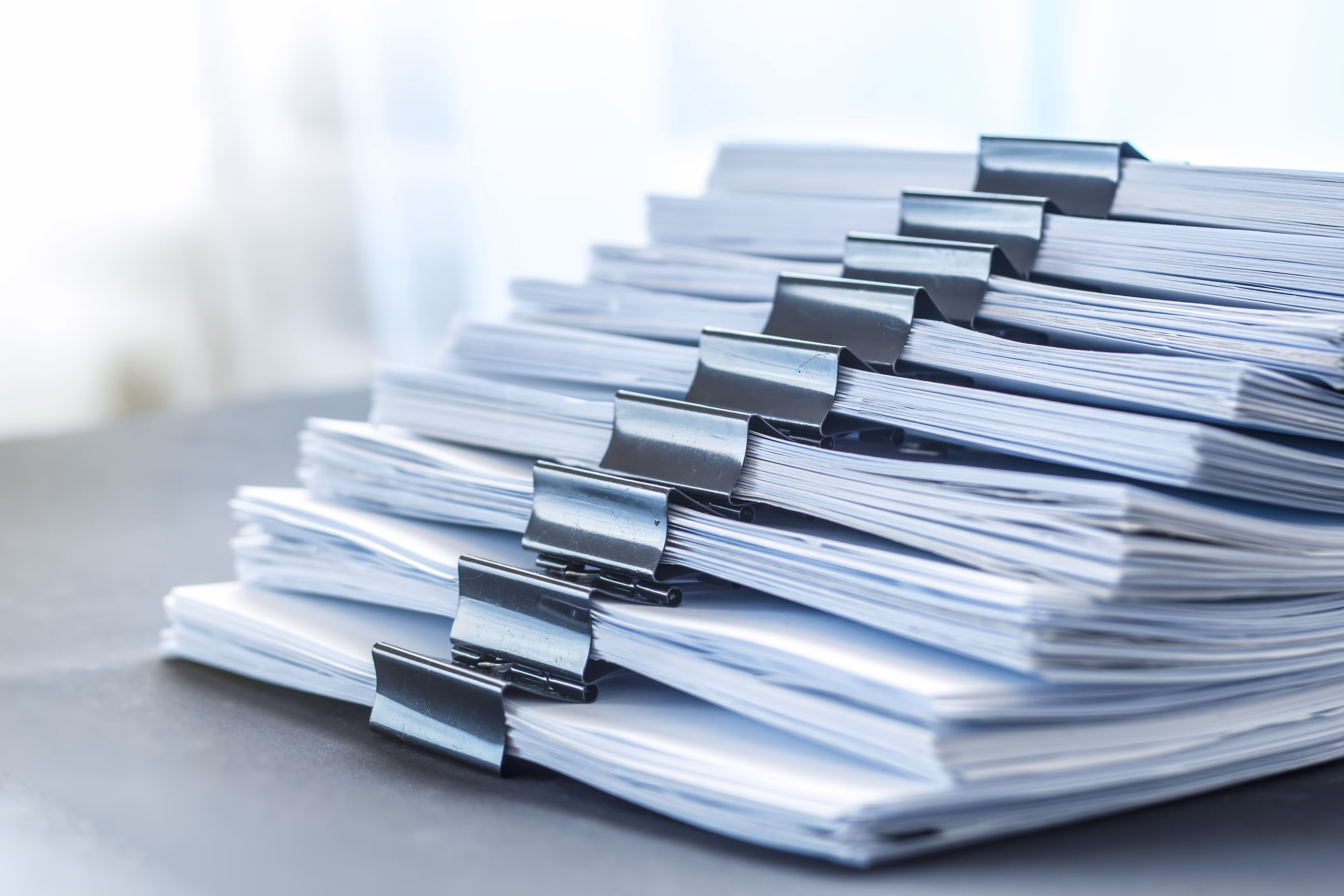 Une pile de documents de bureau organisés en tas avec des pinces métalliques sur une surface grise.