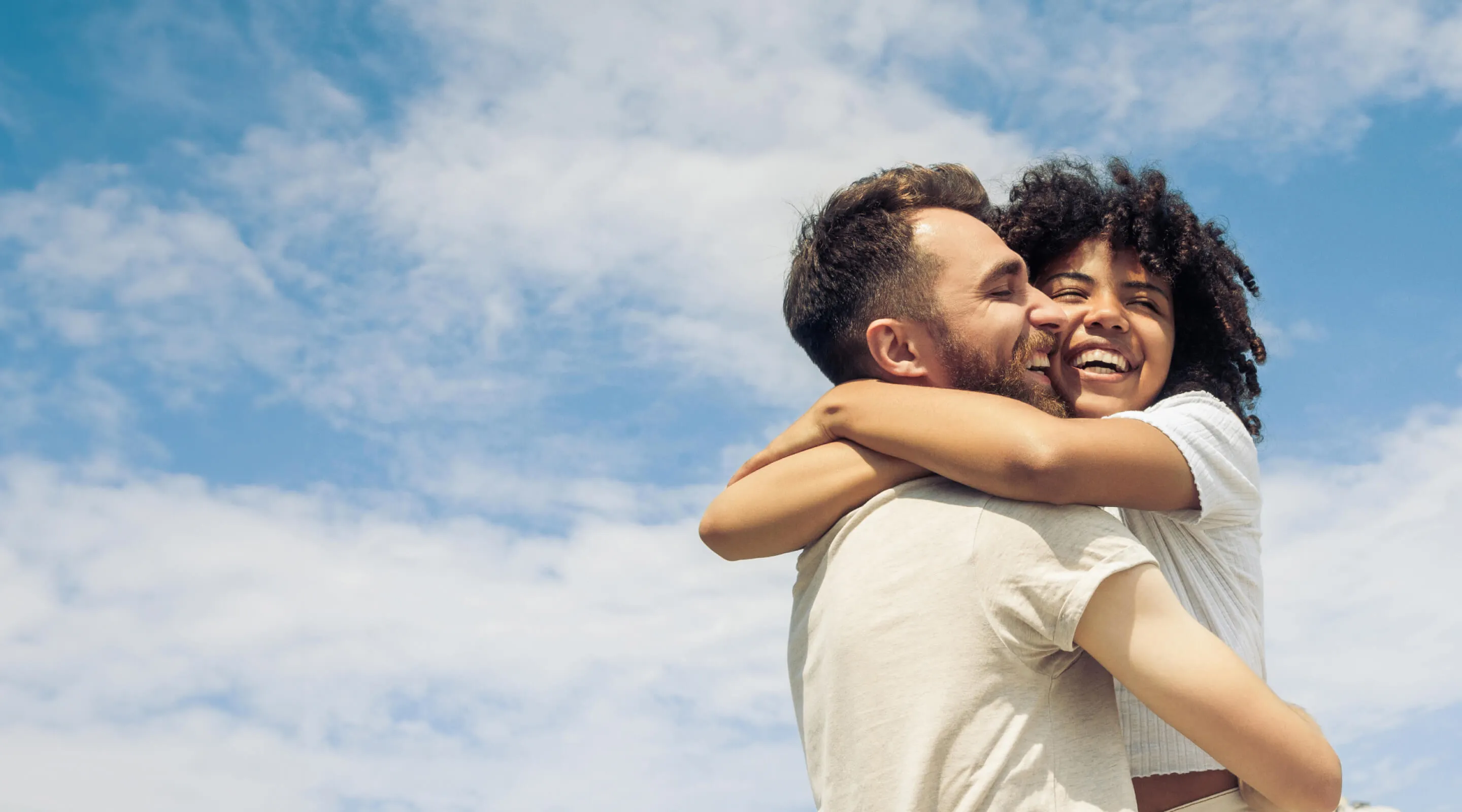 Two people hugging against a blue sky with clouds