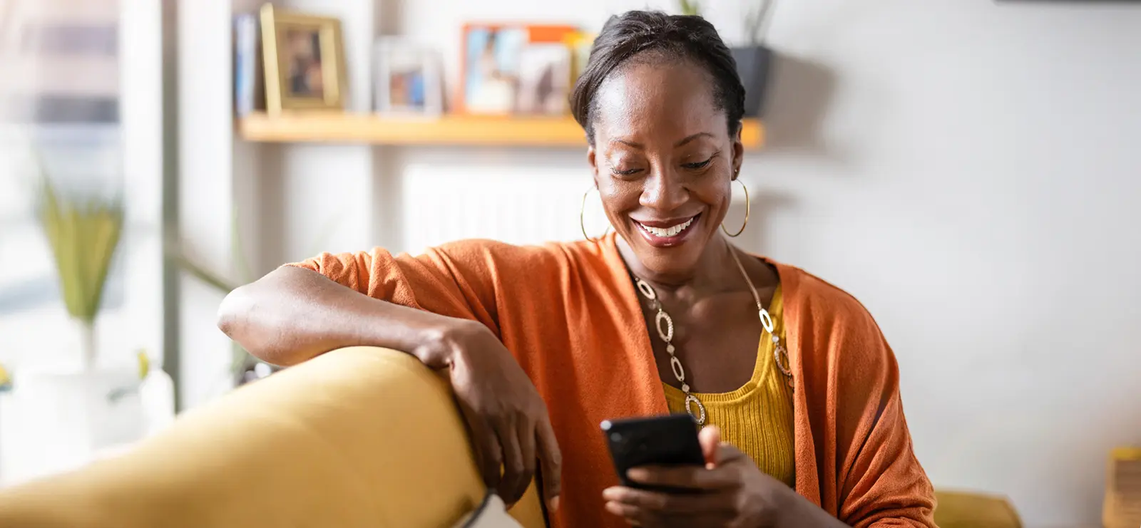 an older woman sitting on her couch smiling down at her phone