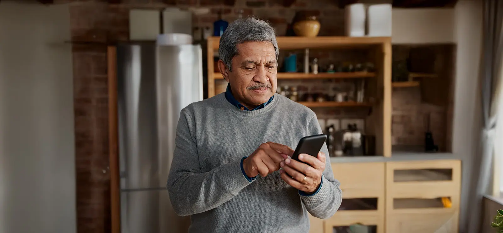 an older gentleman looking at his phone in his kitchen