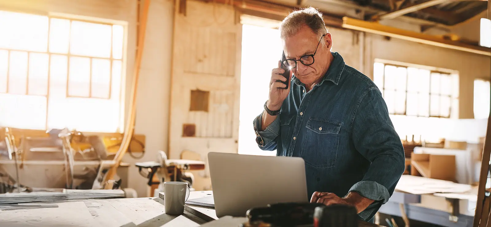 older gentleman talking on the phone while looking at a computer inside his workshop