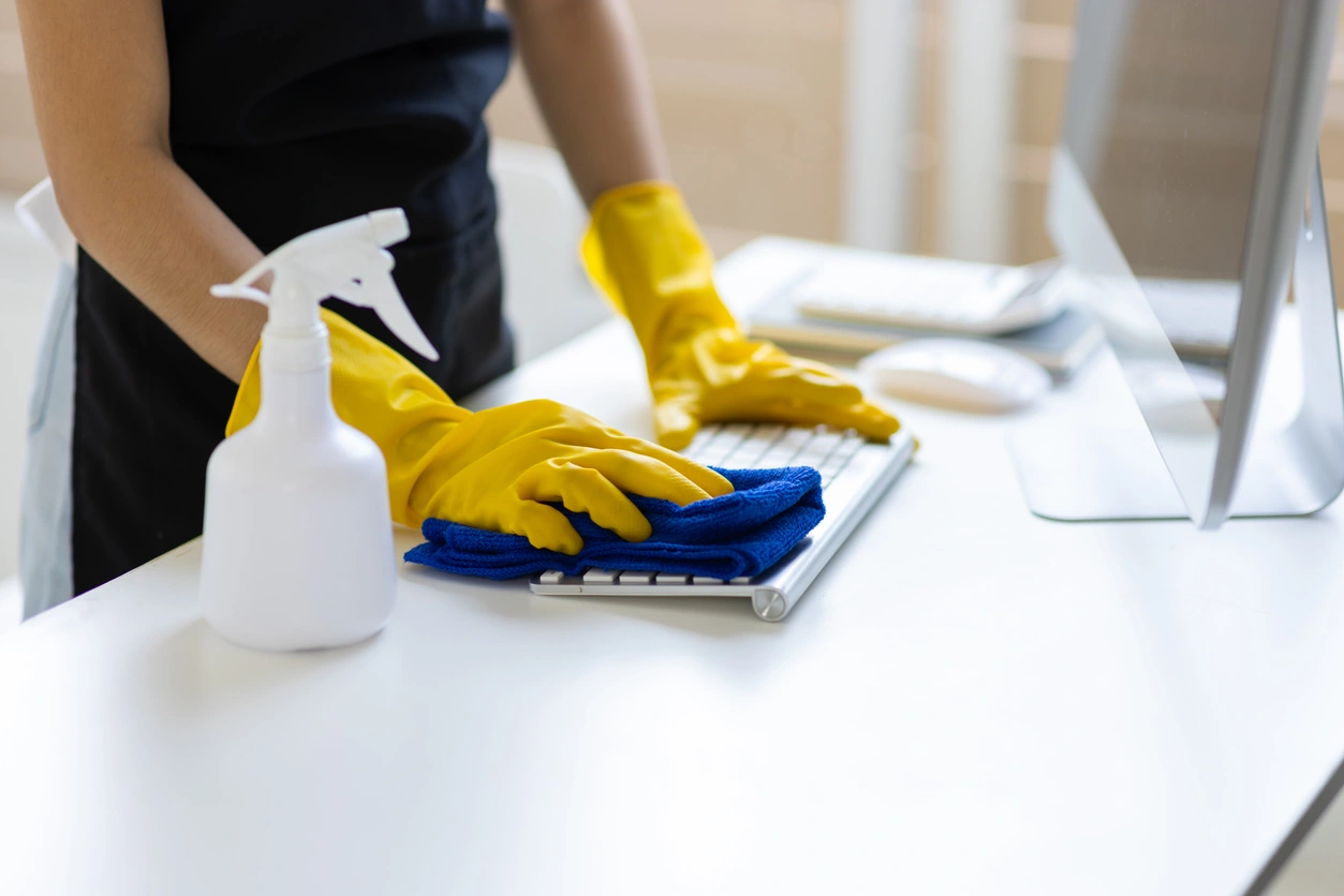 Person cleaning a keyboard with a blue cloth and yellow gloves