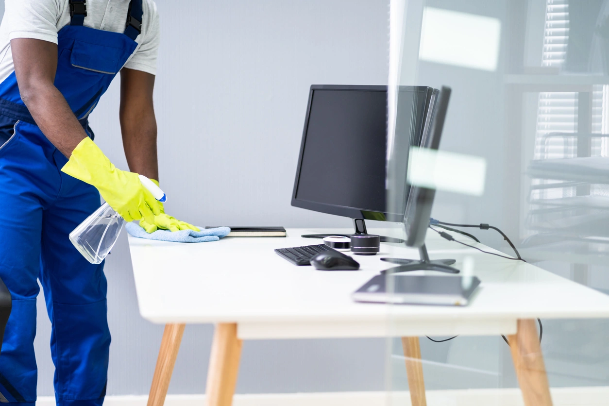 A man in overalls is cleaning a desk with a cloth.