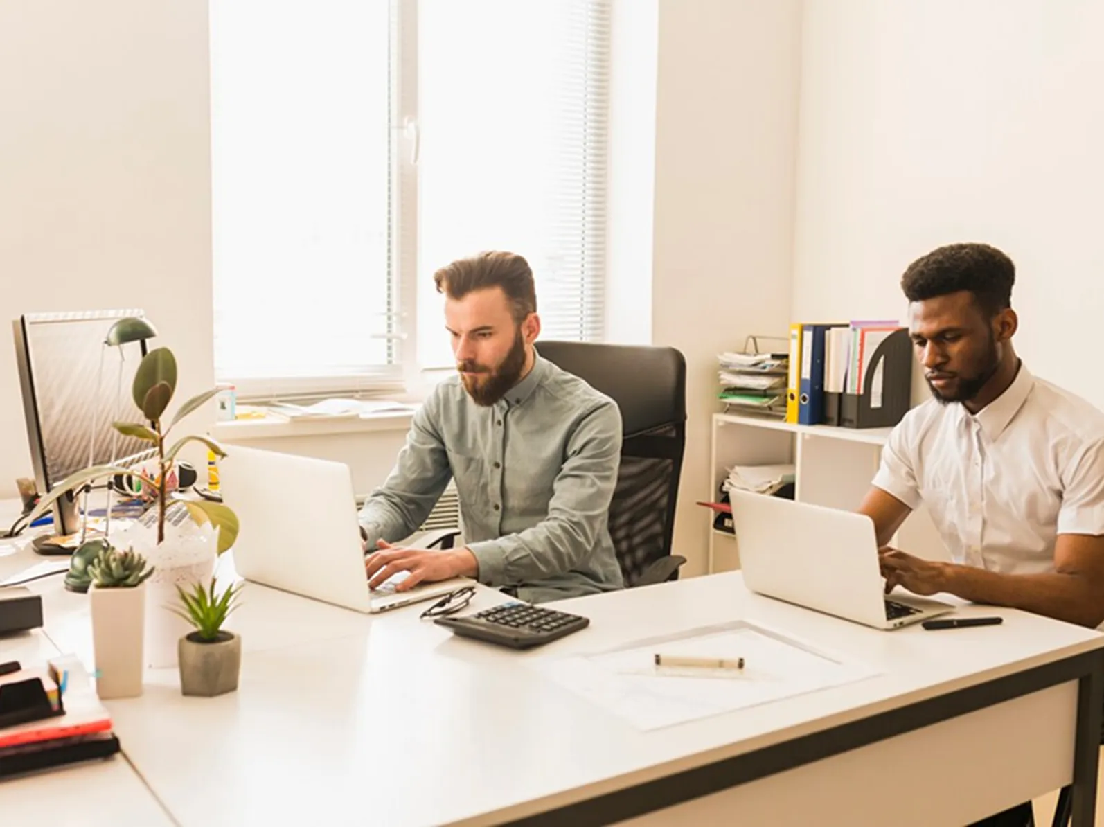 Two men sitting at a desk working on laptops.