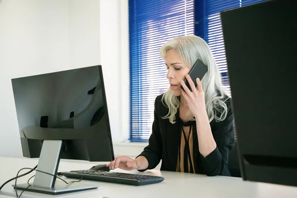 A woman sitting at a desk talking on a cell phone.
