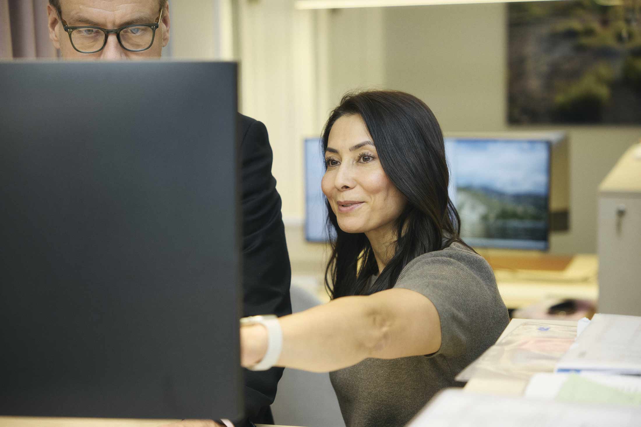 Kvinna pekar på datorskärm medan man tittar noggrant på skärmen i kontorsmiljö.
