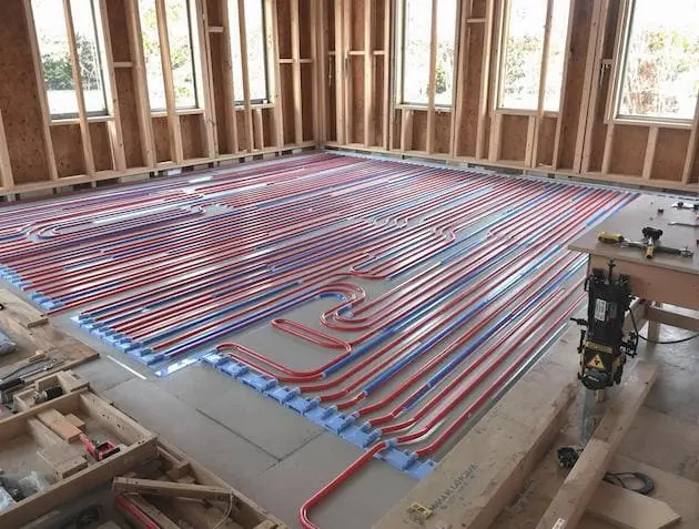 Installation professionnelle d'un plancher chauffant hydraulique : tubes PEX rouges et bleus fixés sur isolant, en cours de pose sur un chantier