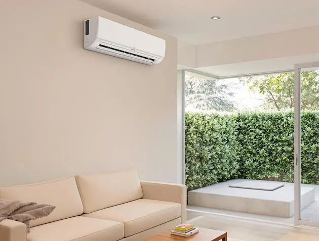 Installation d'une climatisation réversible : unité murale intérieure dans un salon moderne et unité extérieure posée sur une dalle à l'extérieur, entourée d'une haie pour réduire le bruit.