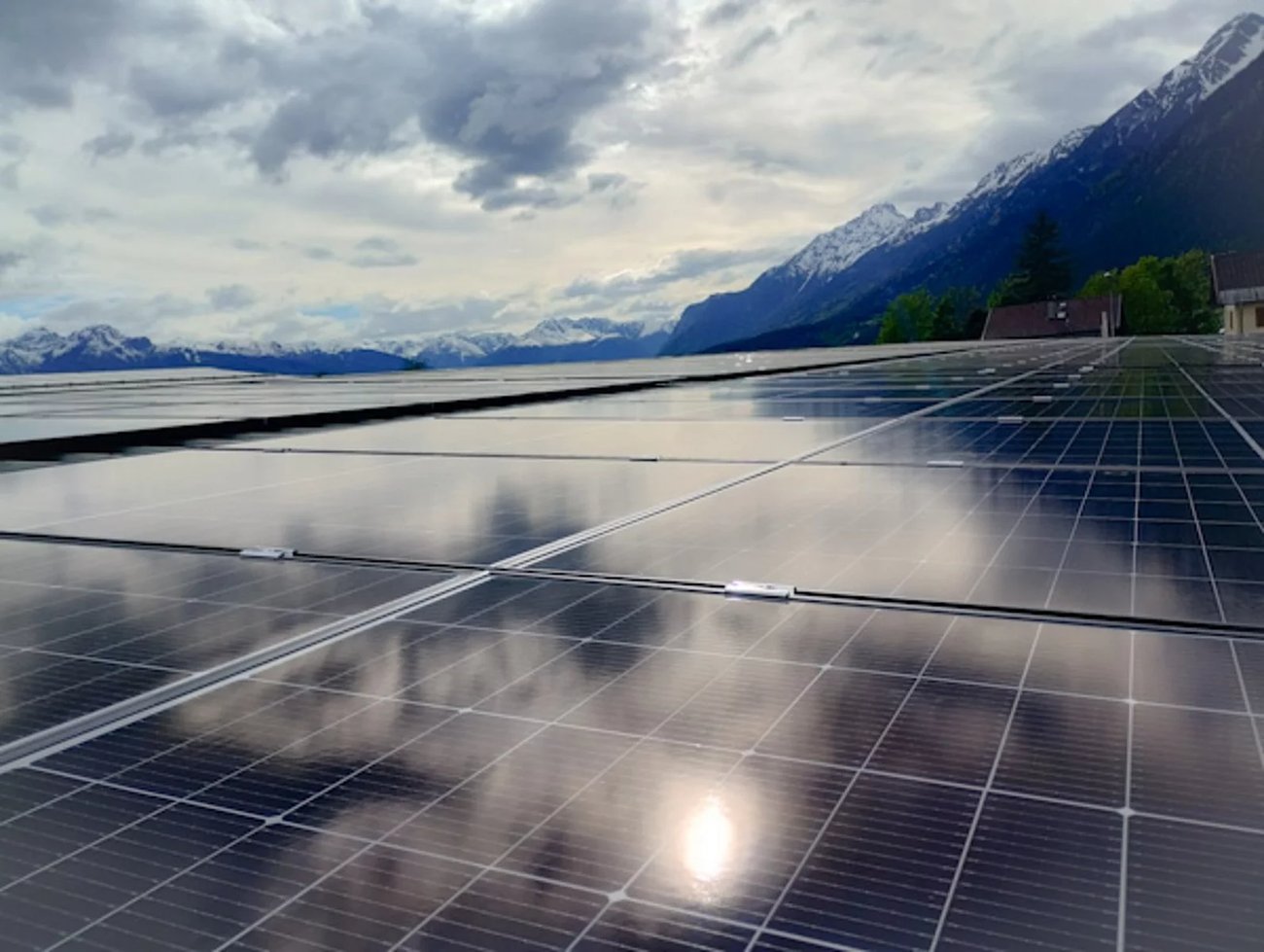 PV-Module auf einem Flachdach in Absam mit Spiegelung der Wolken und Blick auf die Tiroler Alpen