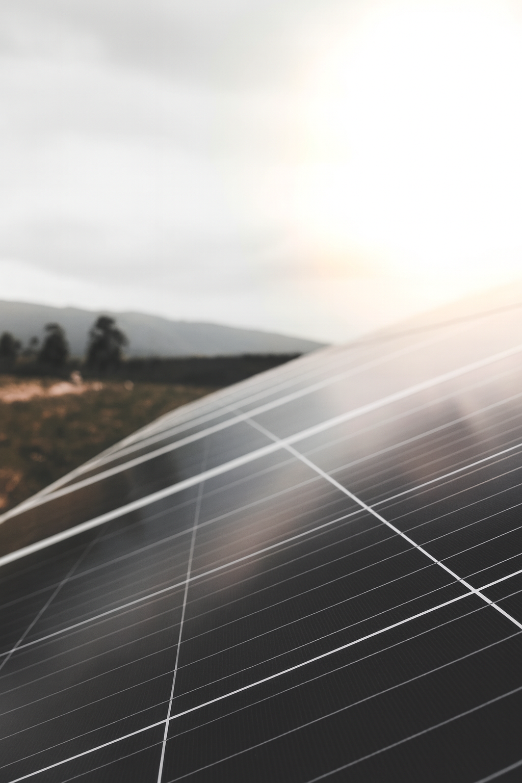 Schrägansicht moderner Solarmodule im Gegenlicht mit Landschaft im Hintergrund, Symbol für nachhaltige Stromproduktion und dezentrale Energieversorgung.