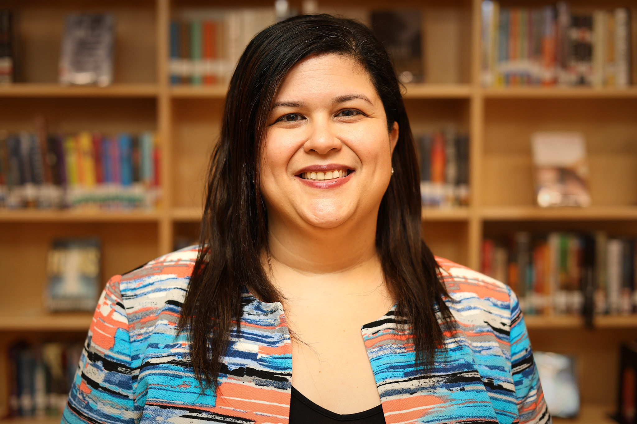 Marleny Martinez smiling in front of school library shelves