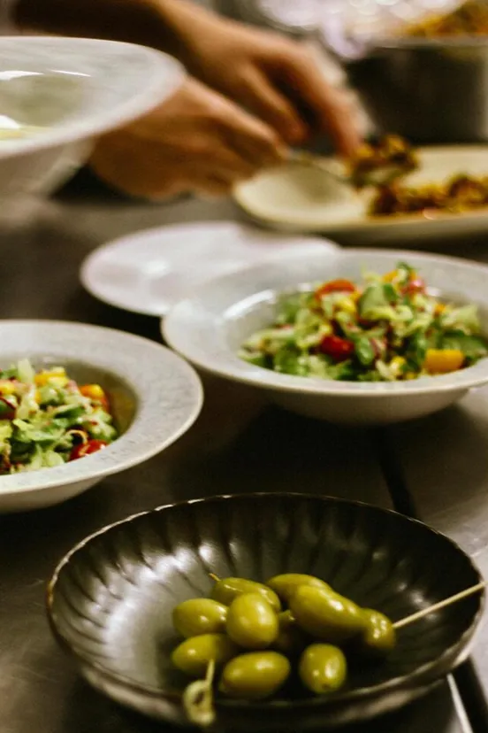 Frische Salate und grüne Oliven werden in der Küche angerichtet und für den Service vorbereitet.